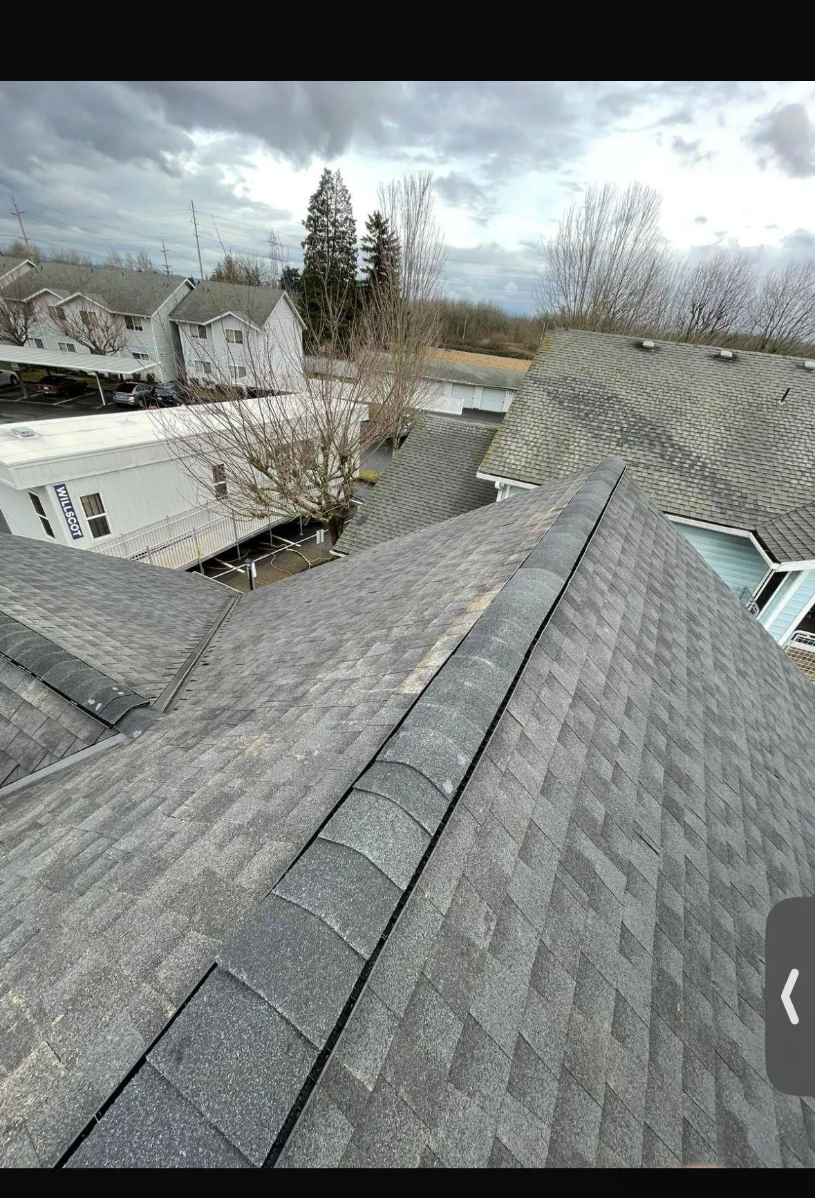 Top view of a residential roof with shingles and cloudy sky.